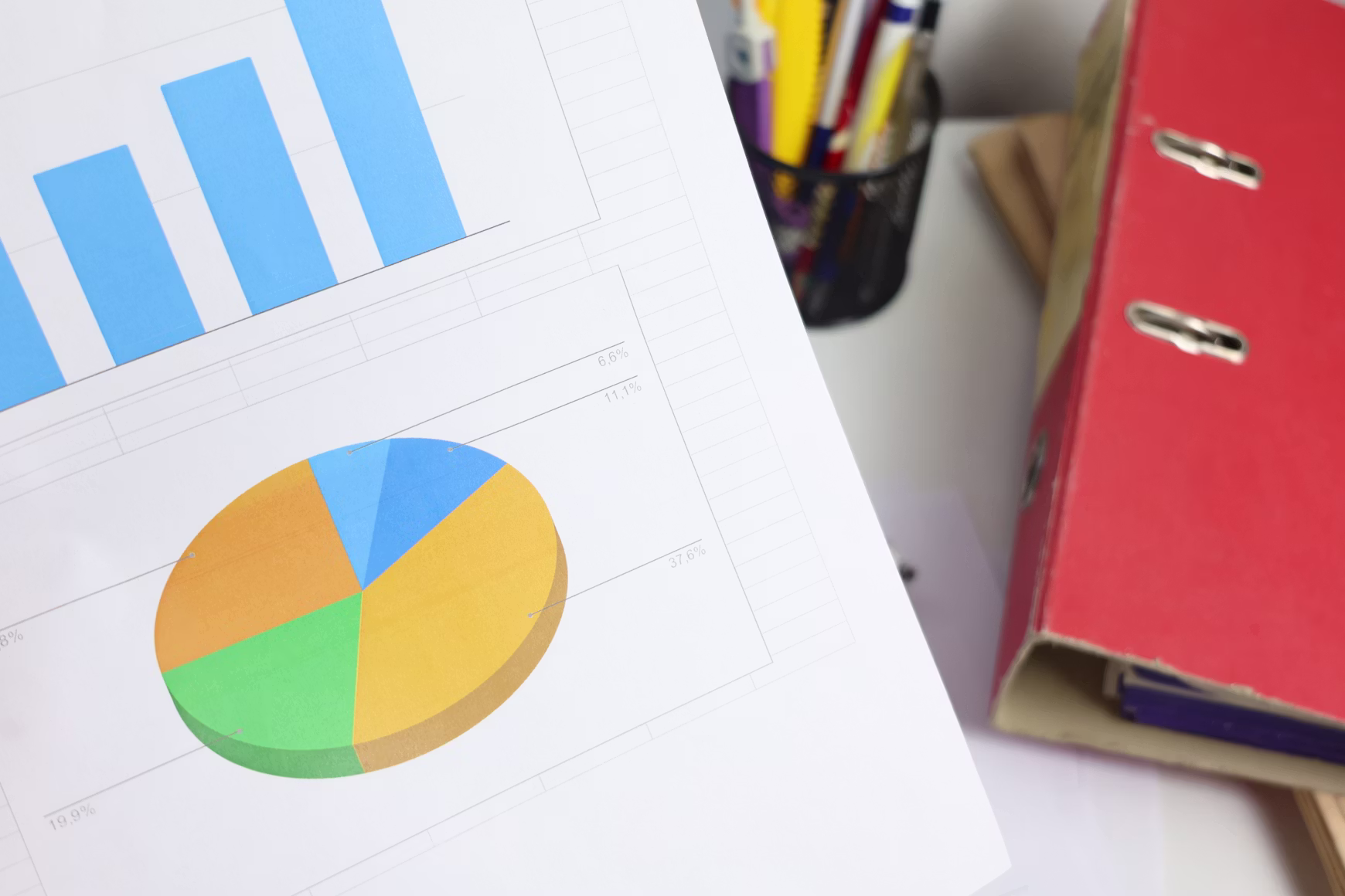 Printed bar and pie charts on a report beside a ring binder.
